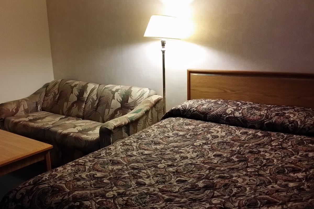 A hotel room with a single bed, a small table, a chair, and a lamp.