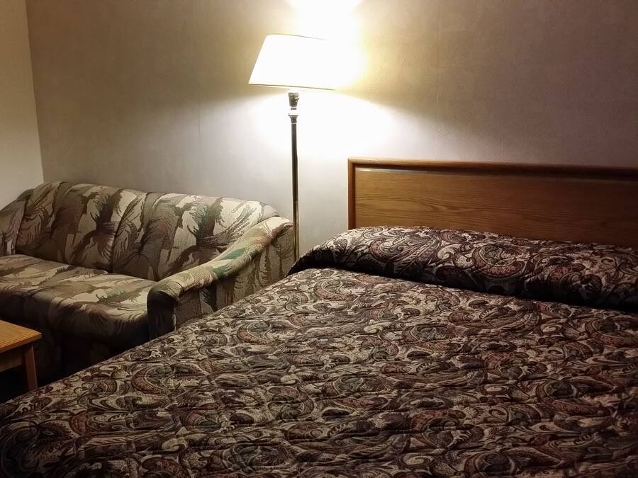 A hotel room with a single bed, a small table, a chair, and a lamp.