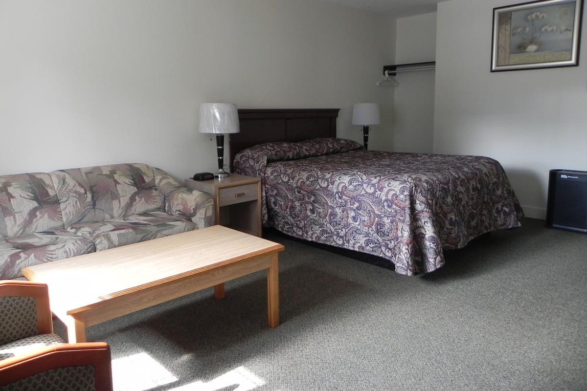 A small, neatly arranged bedroom with a bed, a sofa, a table, and a lamp.