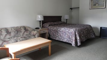 A small, neatly arranged bedroom with a bed, a sofa, a table, and a lamp.