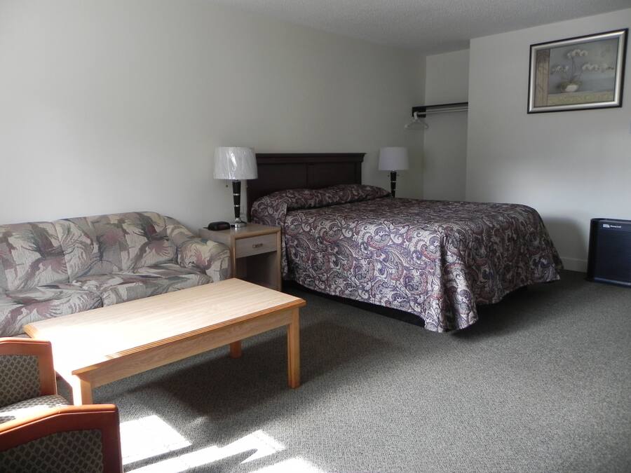 A small, neatly arranged bedroom with a bed, a sofa, a table, and a lamp.