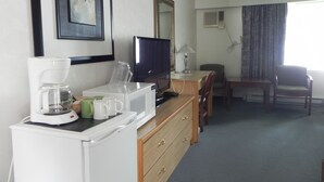A hotel room with a kitchenette, a television, a desk with a chair, and a window with curtains.