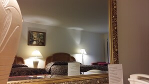 A hotel room with a large mirror, a bed with patterned bedding, two bedside lamps, and a framed painting on the wall.