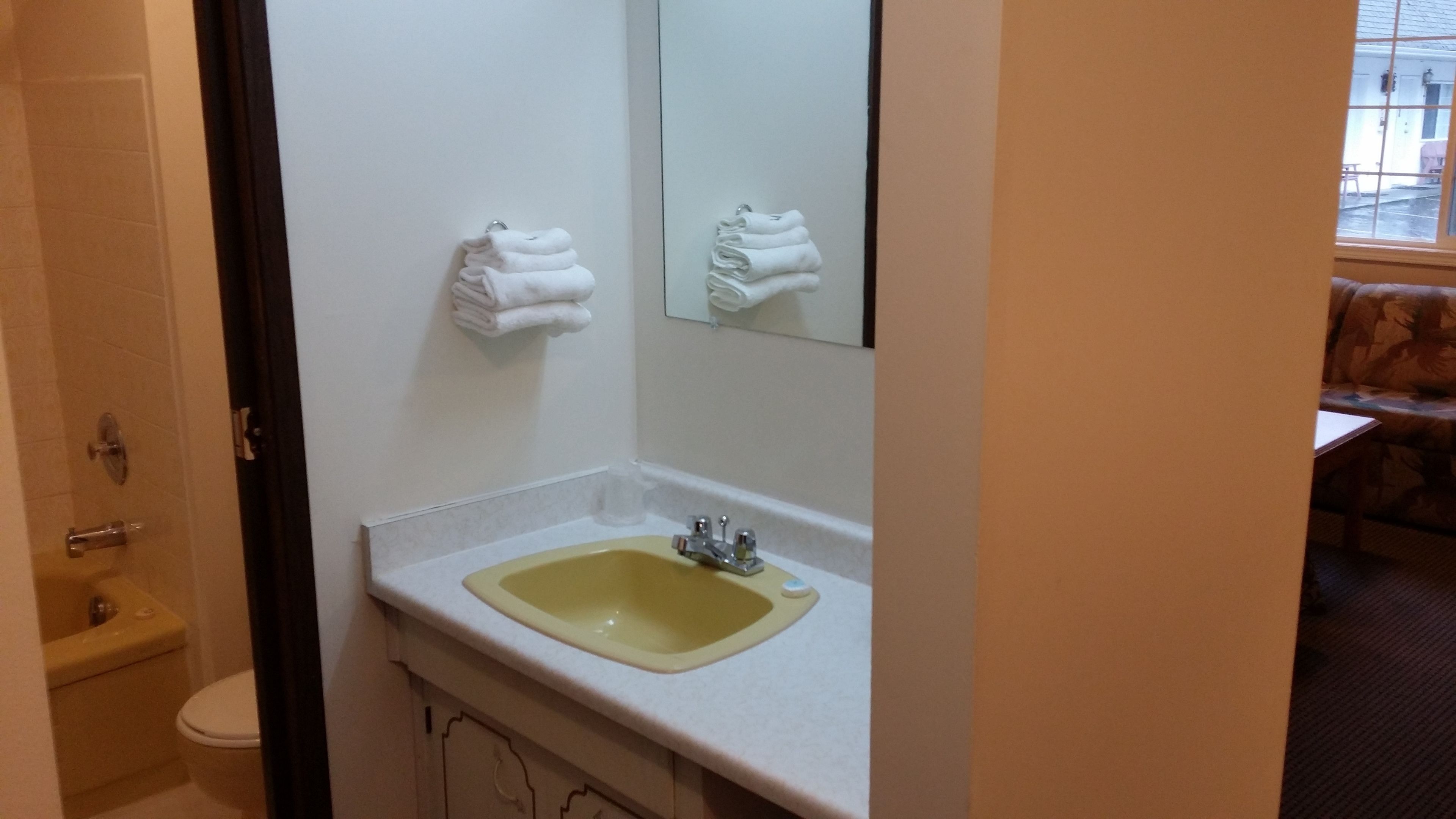 A bathroom with a yellow sink, a toilet, and a towel rack with folded towels.