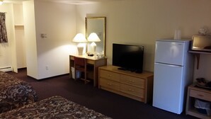 A hotel room with a bed, a desk with a TV, a refrigerator, and a mirror.
