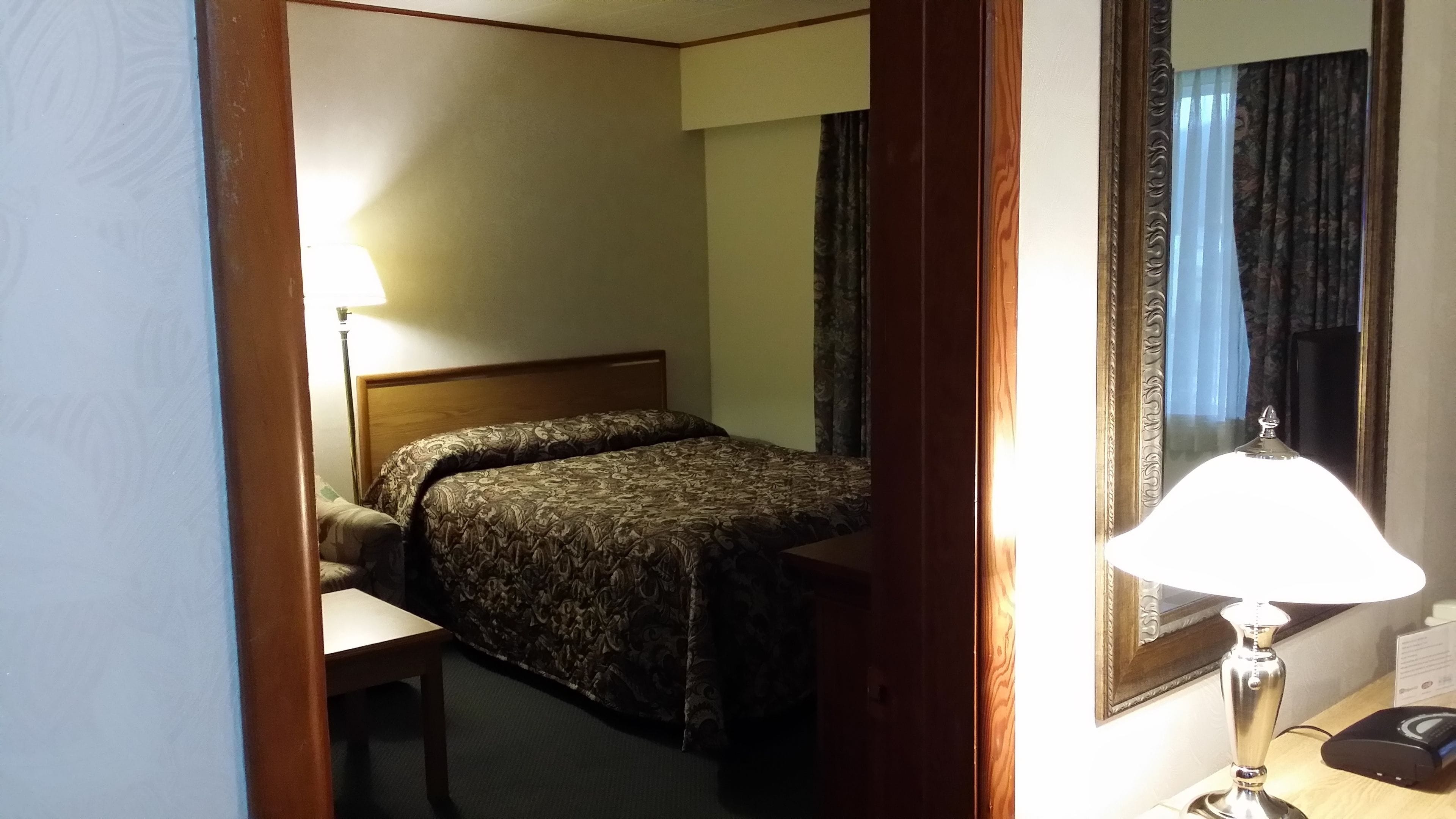 Una habitación de hotel con cama, escritorio, silla, lámpara y espejo.