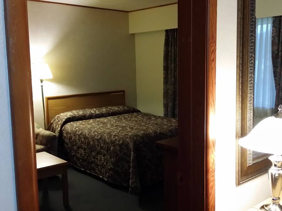 Una habitación de hotel con cama, escritorio, silla, lámpara y espejo.