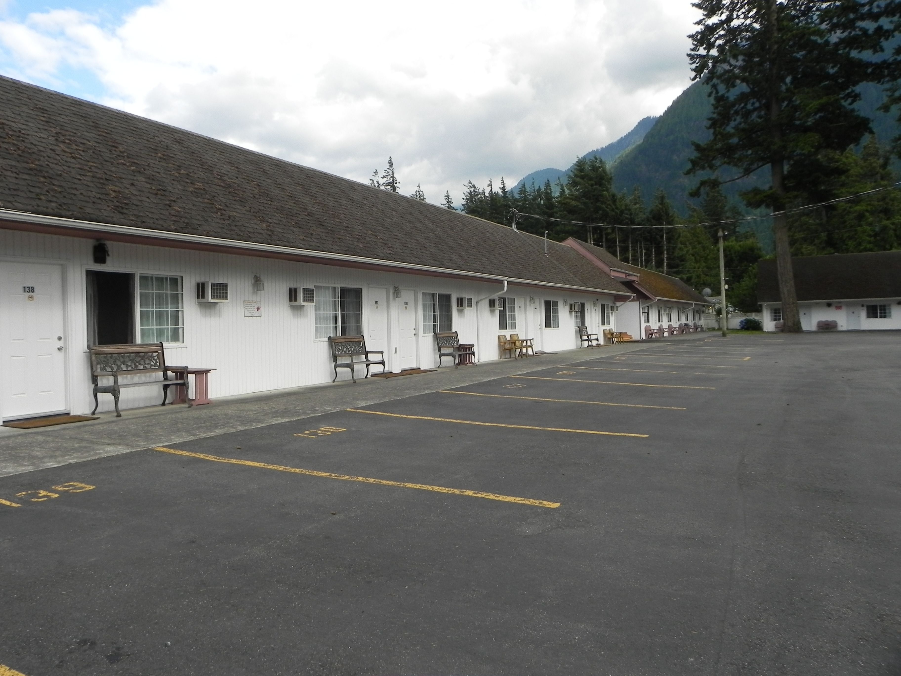 A row of motel rooms with a parking lot in front.