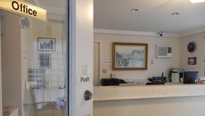 A reception area with a glass door labeled "Office," a push button, a framed picture on the wall, and a desk with a computer and printer.