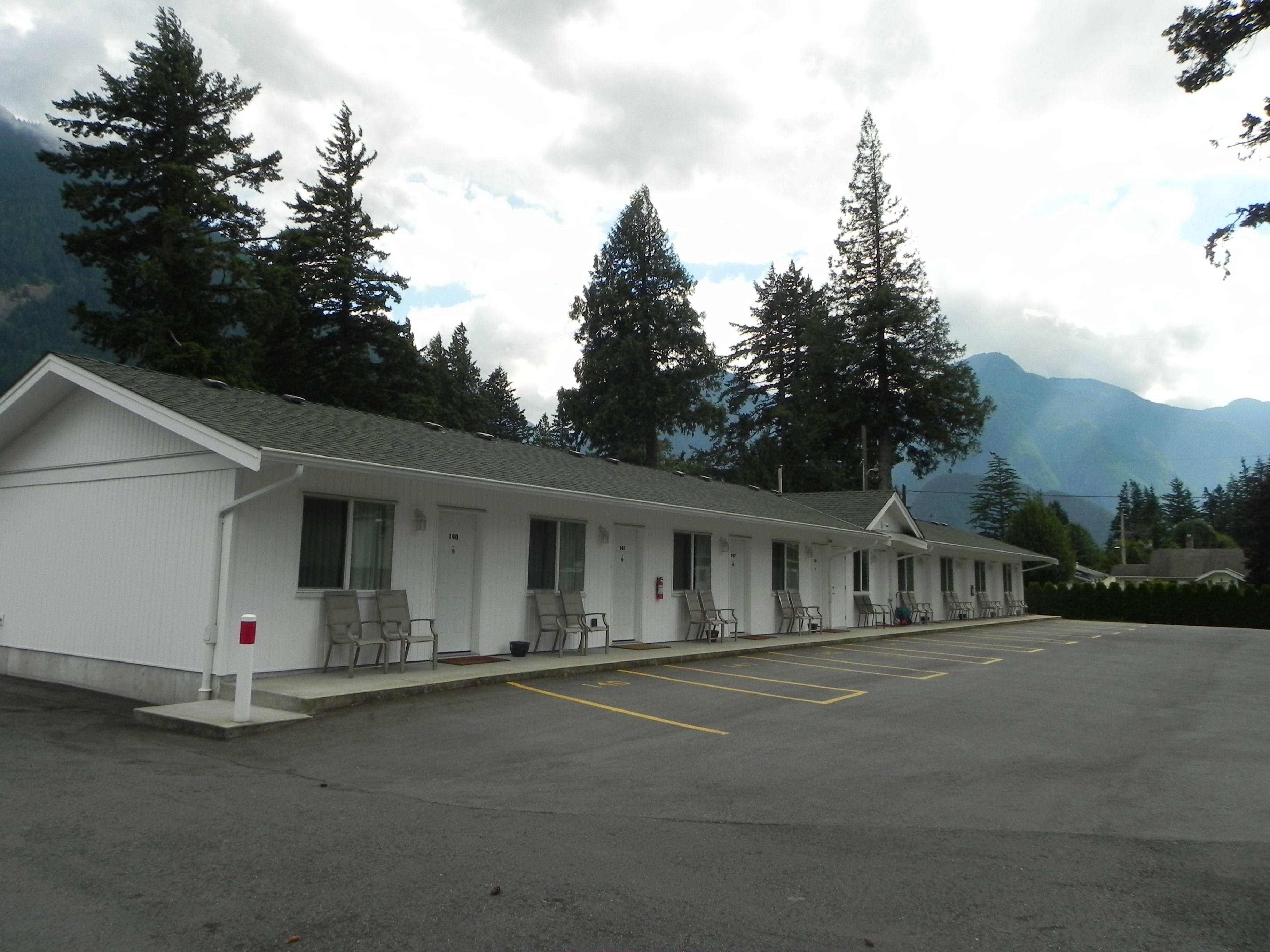 Un motel con una hilera de habitaciones, cada una con ventana y puerta. Hay un estacionamiento al frente.