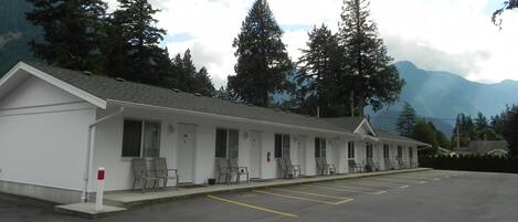 Un motel con una hilera de habitaciones, cada una con ventana y puerta. Hay un estacionamiento al frente.