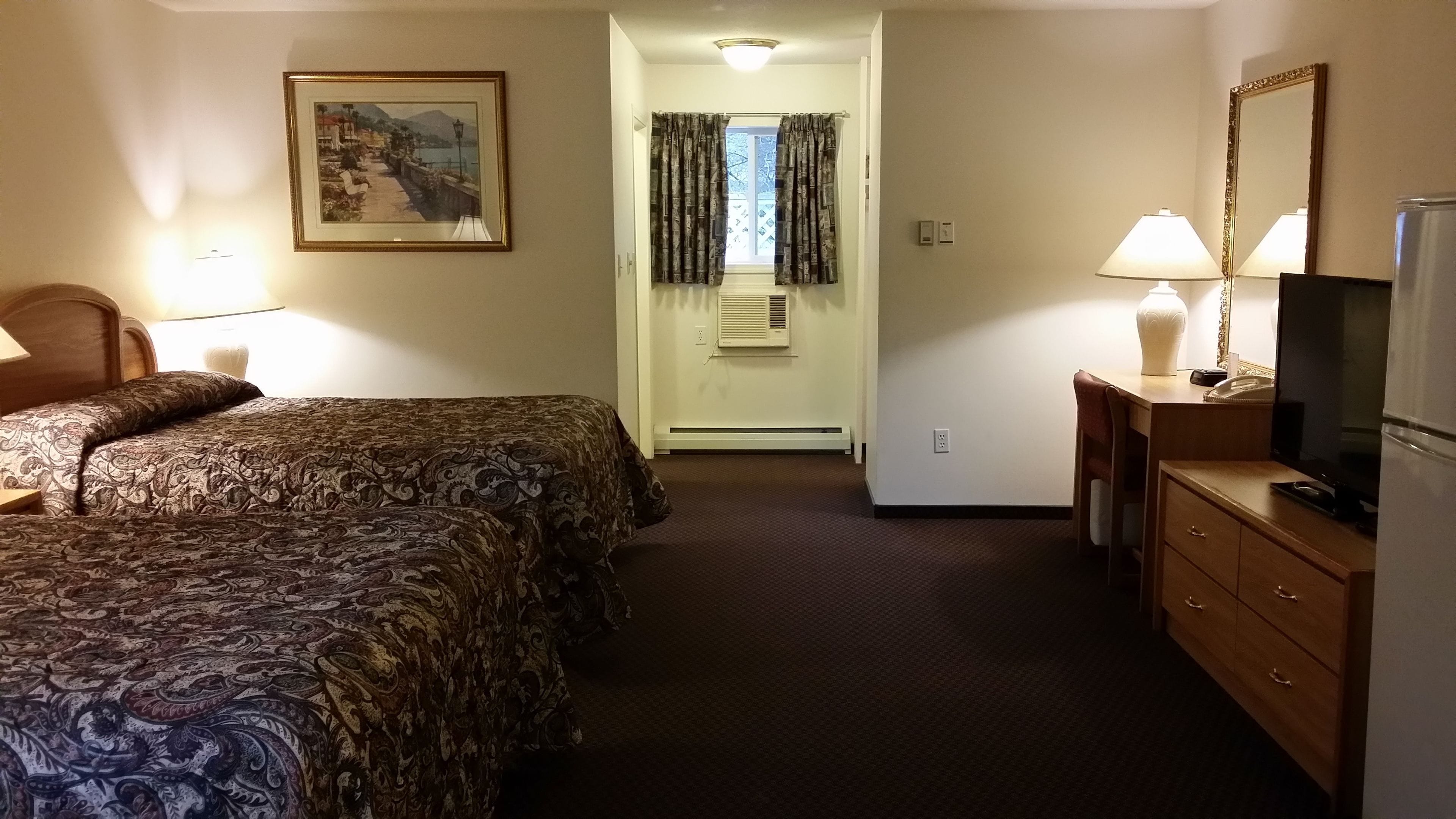 A hotel room with two beds, a television, a dresser, a mirror, a painting on the wall, and a window with curtains.