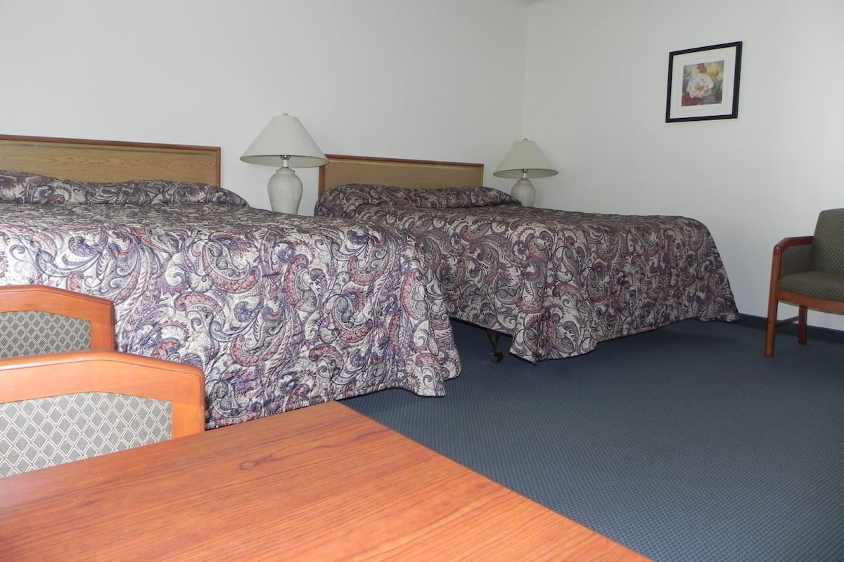 A hotel room with two beds, a wooden table, a chair, and a framed picture on the wall.