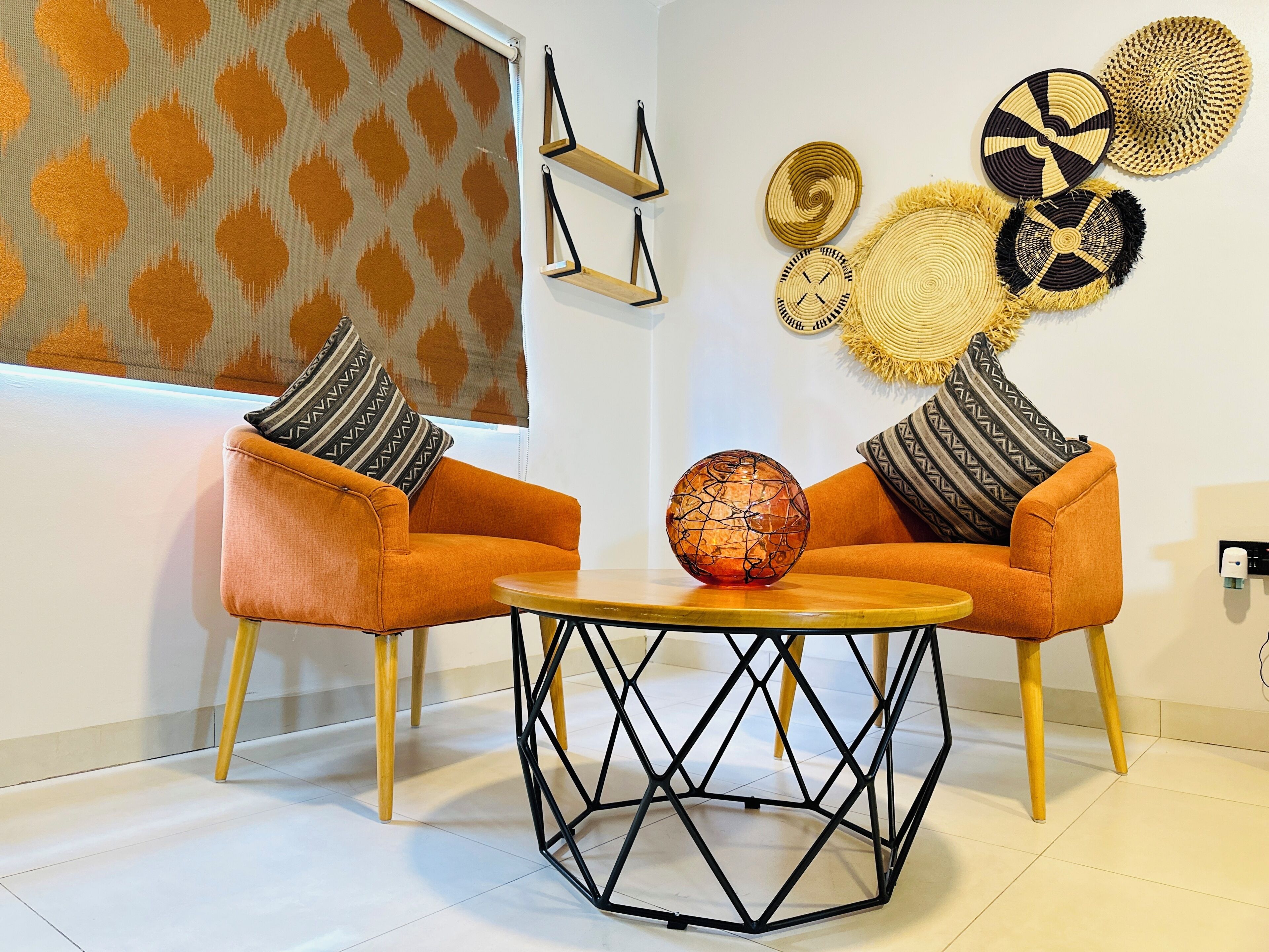Una sala de estar moderna con dos sillones naranja, una mesa de centro redonda y decoración en la pared.