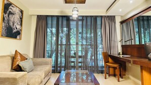 A living room with a sofa, a coffee table, a TV stand, and a large window with curtains. - Fairway Hotel & Spa (Kampala)