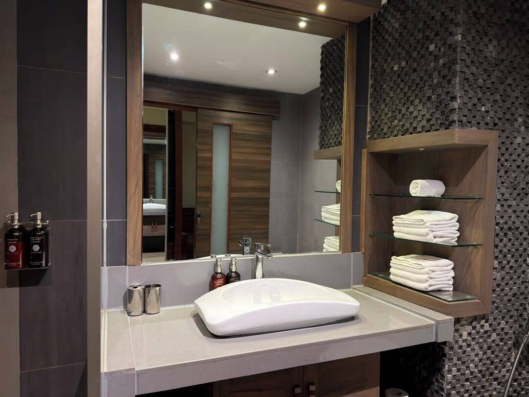 Un baño moderno con un espejo grande, un lavabo blanco y un estante con toallas dobladas.