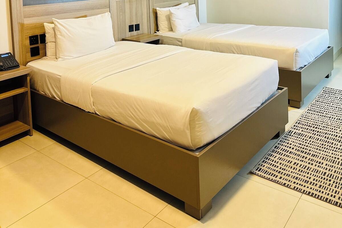 A hotel room with two beds, a nightstand, a phone, decorative wall art, and a ceiling light.