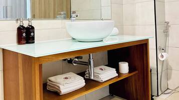 Un baño moderno con un lavamanos grande blanco, tocador de madera y cabina de ducha con mampara de vidrio.