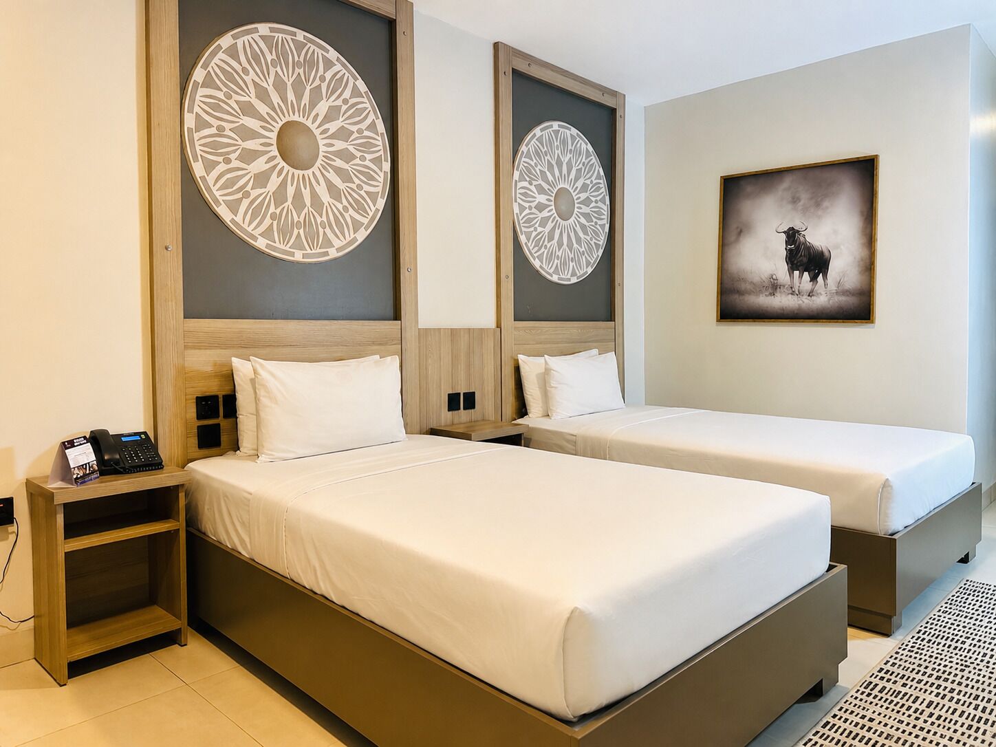 A hotel room with two beds, a phone on the nightstand, and decorative wall panels.