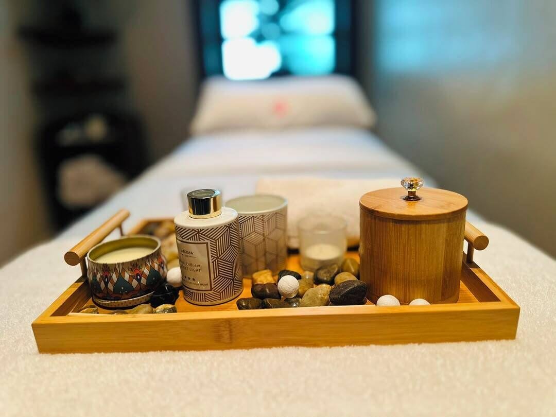 Un plateau en bois contenant divers articles de spa, notamment des bougies, un diffuseur et des pierres, posé sur une serviette blanche.