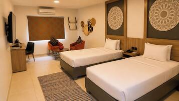 A hotel room with two beds, a desk, a chair, a TV, and decorative wall art.