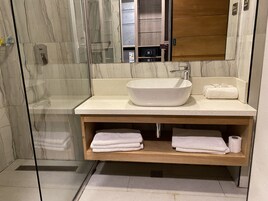 Un baño moderno con un lavamanos grande tipo recipiente, tocador de madera y cabina de ducha con mampara de vidrio.