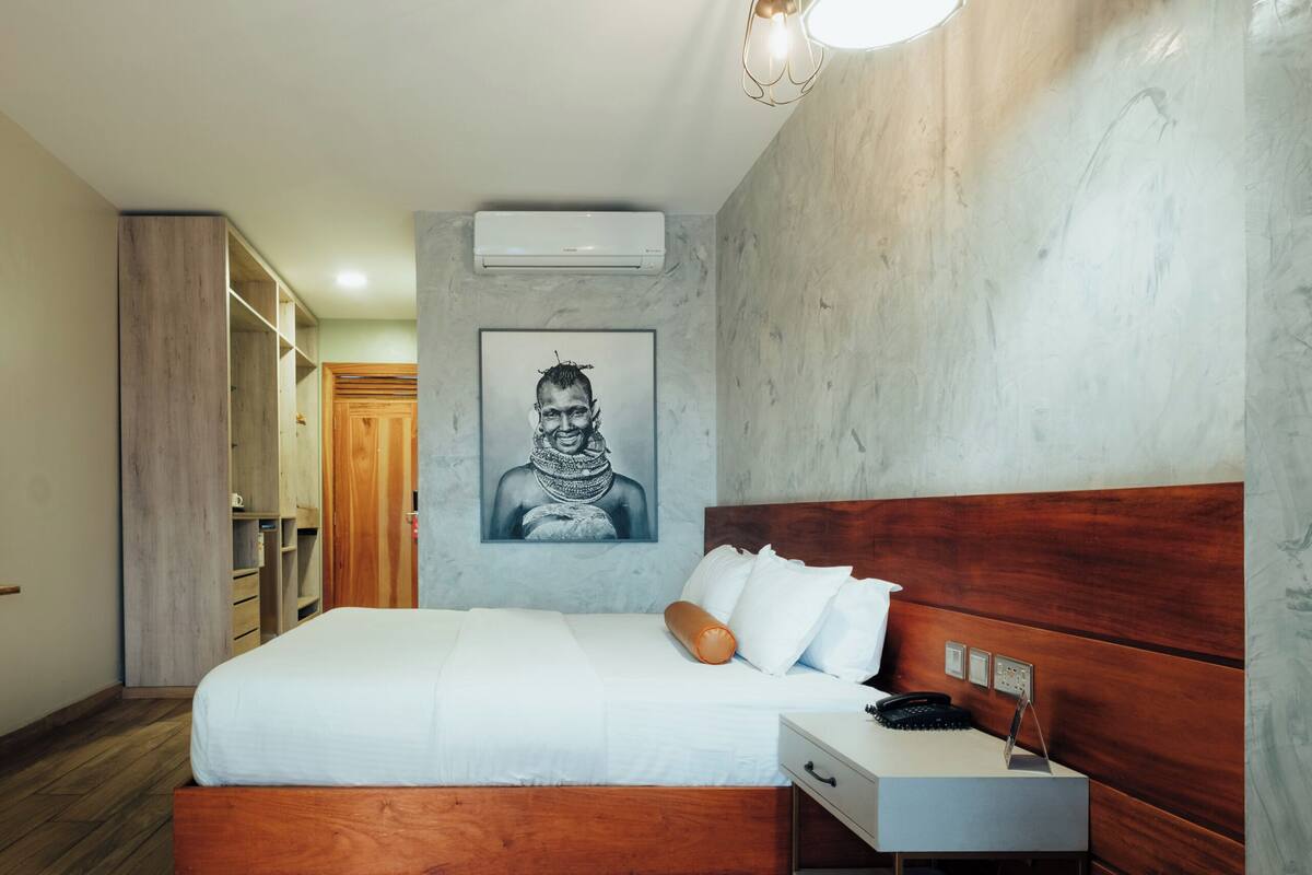 A bedroom with a wooden bed, a nightstand, a desk, a wardrobe, and an air conditioning unit.