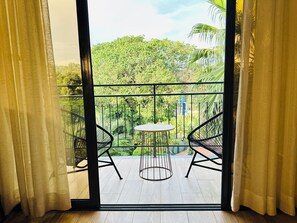 A balcony with a table and two chairs, a view of greenery, and a building in the background. - Fairway Hotel & Spa (Kampala)