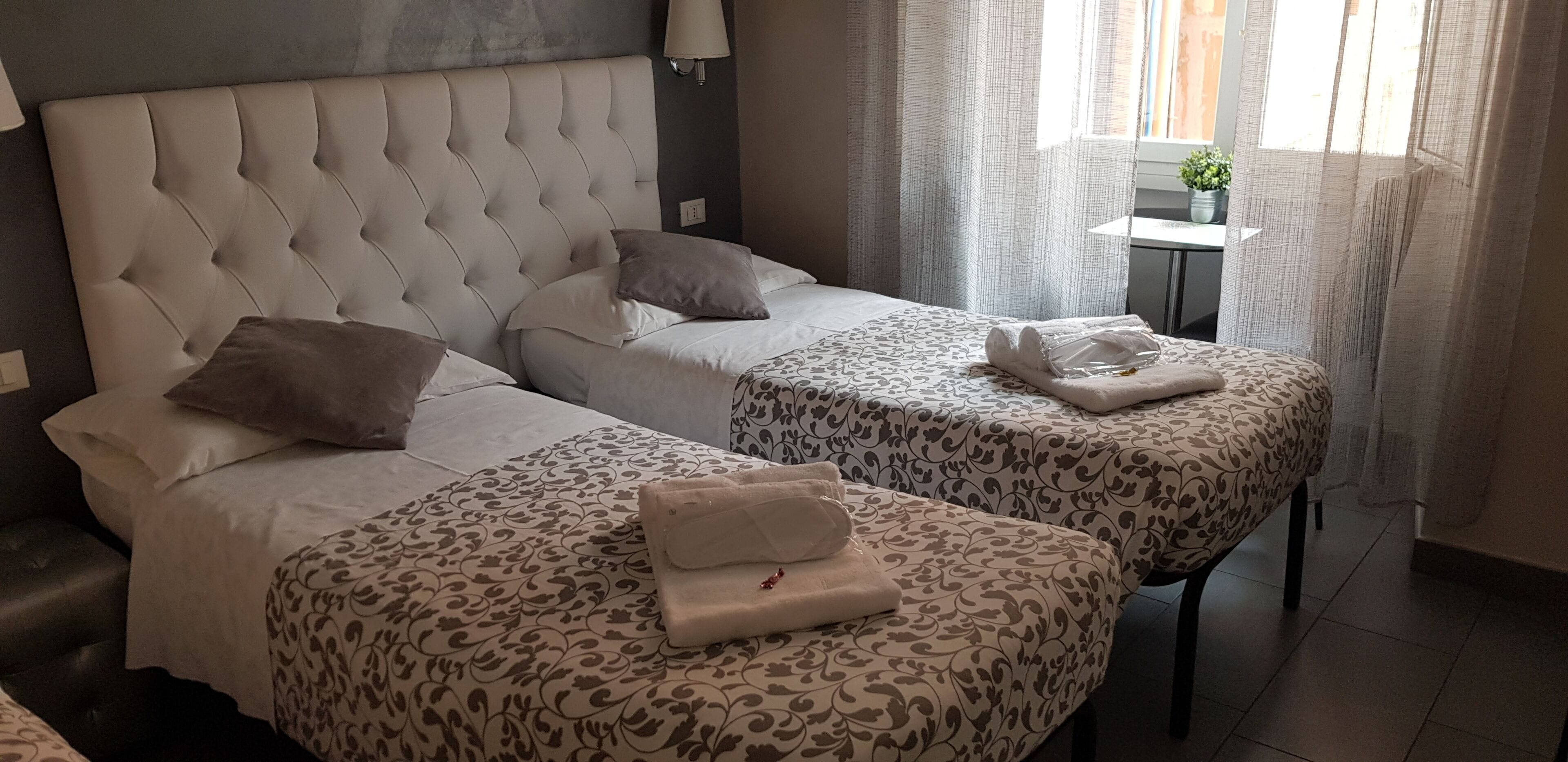 Een hotelkamer met twee bedden, een hoofdeinde, een nachtkastje en een raam met gordijnen.
