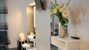 A bathroom with a white vanity, a mirror, a sink, and a vase of flowers on a shelf. - Relais Cavour Inn (Rome)