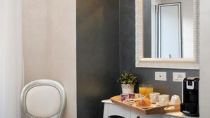 A small bathroom with a white chair, a vanity with a mirror, a sink, and a trash bin. - Relais Cavour Inn (Rome)