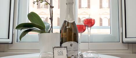 A table with a bottle of wine, a glass, a tray with a dessert, and a card on a white table near a window with a view of buildings.