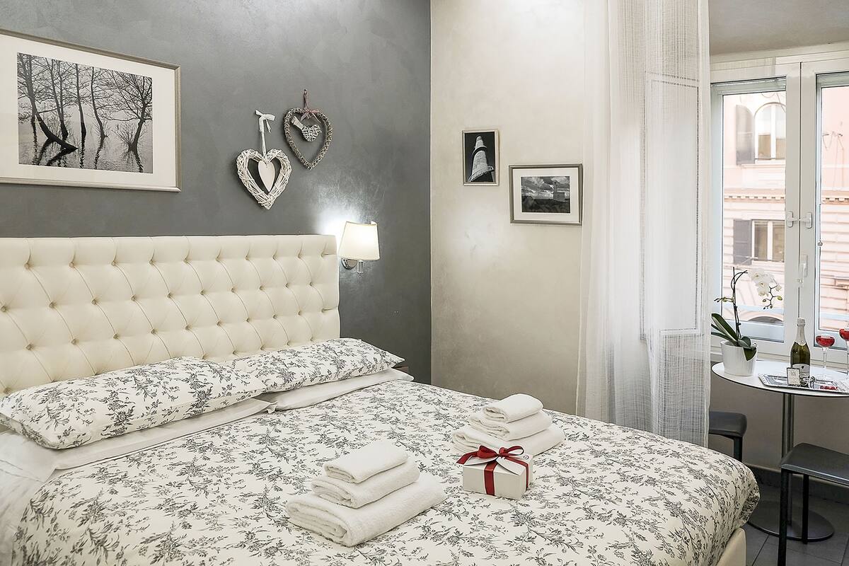 A neatly made bed with floral bedding, a heart-shaped wall decoration, and a framed picture.