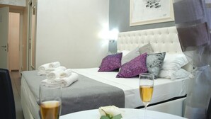 A hotel room with a neatly made bed, a bedside table with a glass of wine and a flower, and a painting on the wall. - Relais Cavour Inn (Rome)