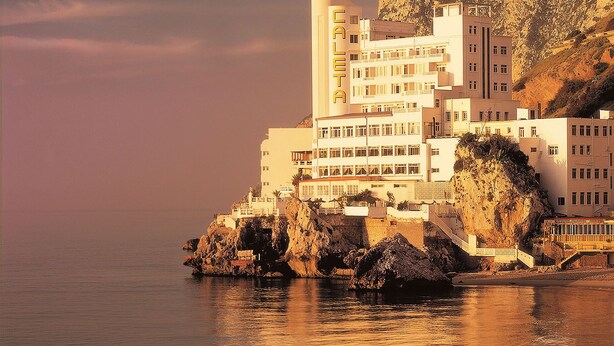 A coastal hotel with multiple floors, a rocky cliff, and boats on the beach. - The Caleta Hotel Health, Beauty & Conference Centre (Gibraltar)