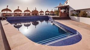A swimming pool with a curved edge, sun umbrellas, lounge chairs, and a building with a white facade. - The Caleta Hotel Health, Beauty & Conference Centre (Gibraltar)