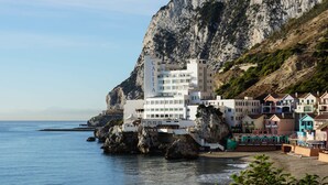 A coastal hotel with multiple buildings, including a prominent white structure with balconies, situated by the sea with rocky cliffs in the background. - The Caleta Hotel Health, Beauty & Conference Centre (Gibraltar)