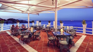 An outdoor terrace with tables and chairs, overlooking a body of water. - The Caleta Hotel Health, Beauty & Conference Centre (Gibraltar)