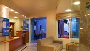 A hotel lobby with a reception desk, a sofa, a dining area, and a large window with a view. - Radamanthy's Apartments (Rethymno)