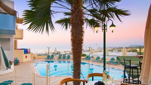 A rooftop pool area with lounge chairs, a palm tree, and a table with a bottle and fruit. - Radamanthy's Apartments (Rethymno)