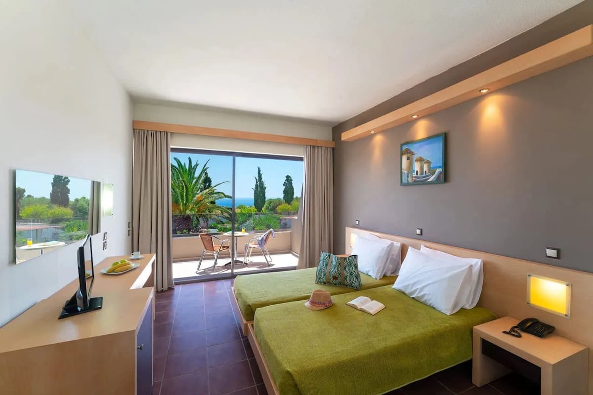 A hotel room with two beds, a balcony with a table and chairs, and a painting on the wall.
