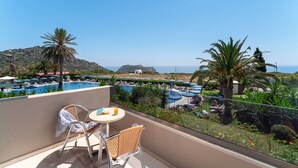 A balcony with a table and chairs overlooking a pool area with umbrellas and palm trees. - Cathrin Hotel Rhodes By Anayia All Inclusive Resorts (Rhodes)