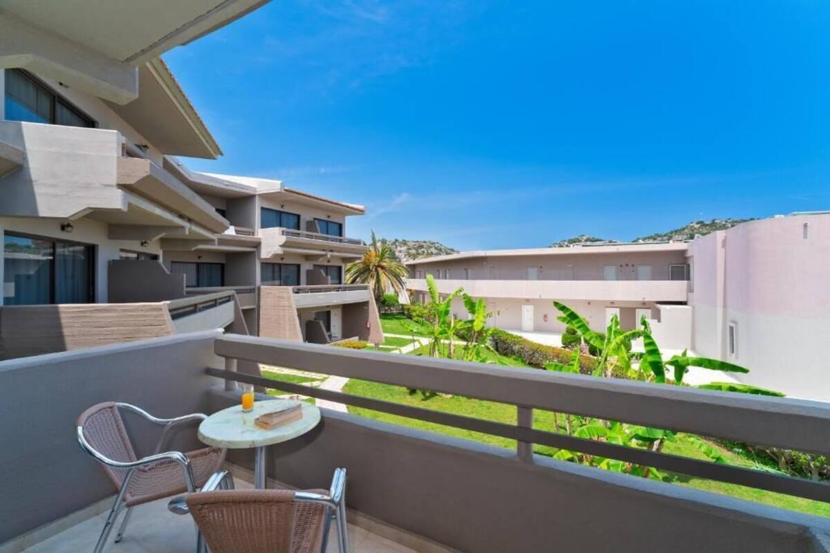 A balcony with two wicker chairs and a small round table, overlooking a landscaped garden and a building complex.