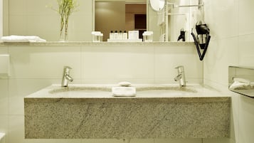 A bathroom with a granite countertop sink, two faucets, a mirror, and a hairdryer mounted on the wall.