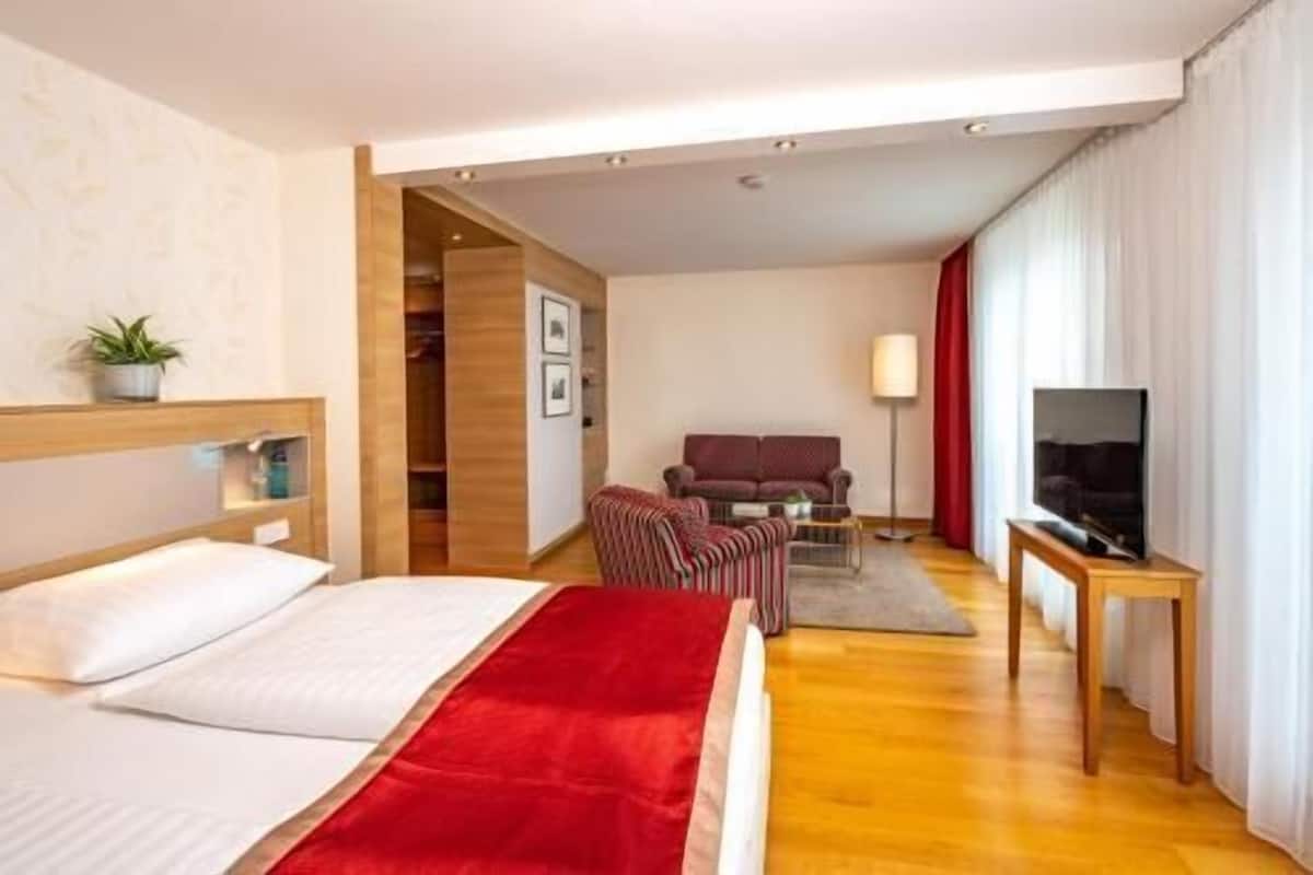 Ein Hotelzimmer mit Bett, Fernseher, Sofa und Schreibtisch.