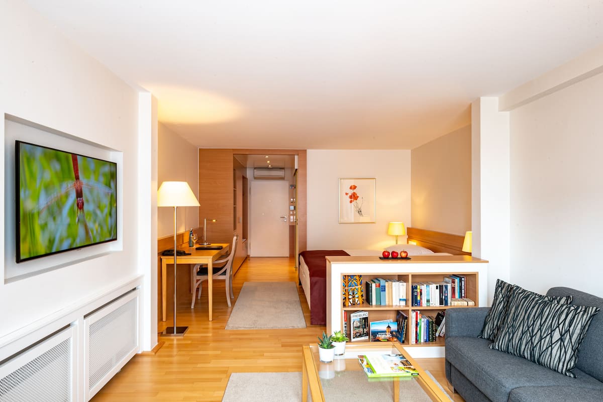 Ein modernes Wohnzimmer mit Flachbildfernseher, einer Couch, einem Couchtisch, einem Bücherregal und einem Essbereich mit Tisch und Stühlen.