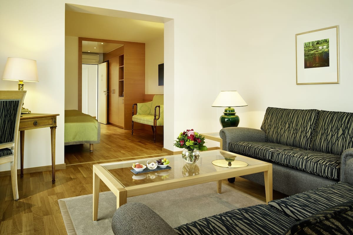 Ein modernes Wohnzimmer mit einer Couch, einem Sessel, einem Couchtisch und Lampen. Eine Tür führt in einen anderen Raum.