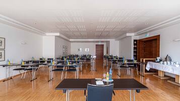 Un salón de conferencias con varias mesas y sillas, piso de madera y techo blanco con iluminación empotrada.