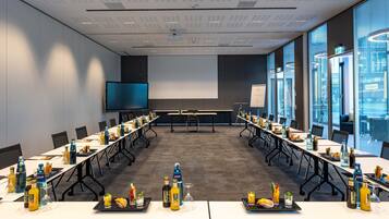 Ein Konferenzraum mit langem Tisch, Stühlen, einer Projektionsleinwand und einem großen Fenster.