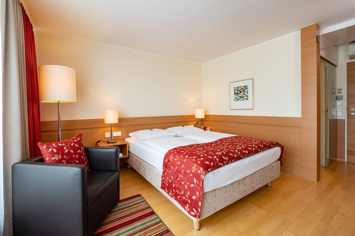 Ein Hotelzimmer mit einem Bett, einem Nachttisch, einer Lampe, einem Sofa und einem roten Vorhang.